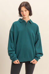 woman wearing a dark teal oversized polo sweatshirt with a collared neckline and long sleeves