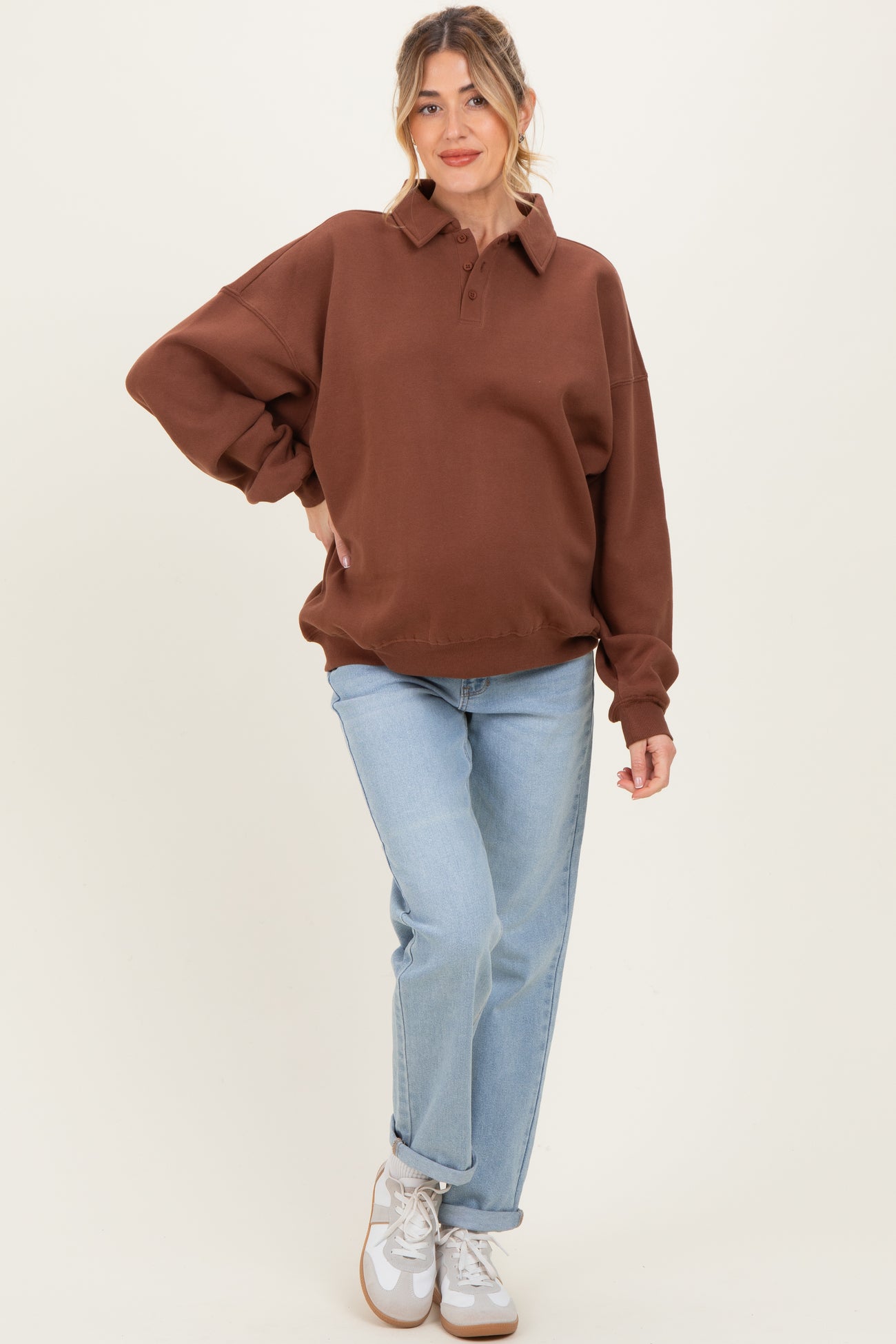woman wearing a brown oversized polo sweatshirt as maternity wear with a visible baby bump and light blue jeans