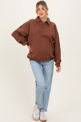 woman wearing a brown oversized polo sweatshirt as maternity wear with a visible baby bump and light blue jeans