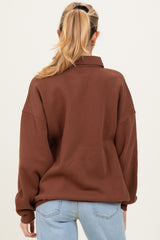 woman wearing a brown oversized maternity sweatshirt, view from the back, with light blue jeans.