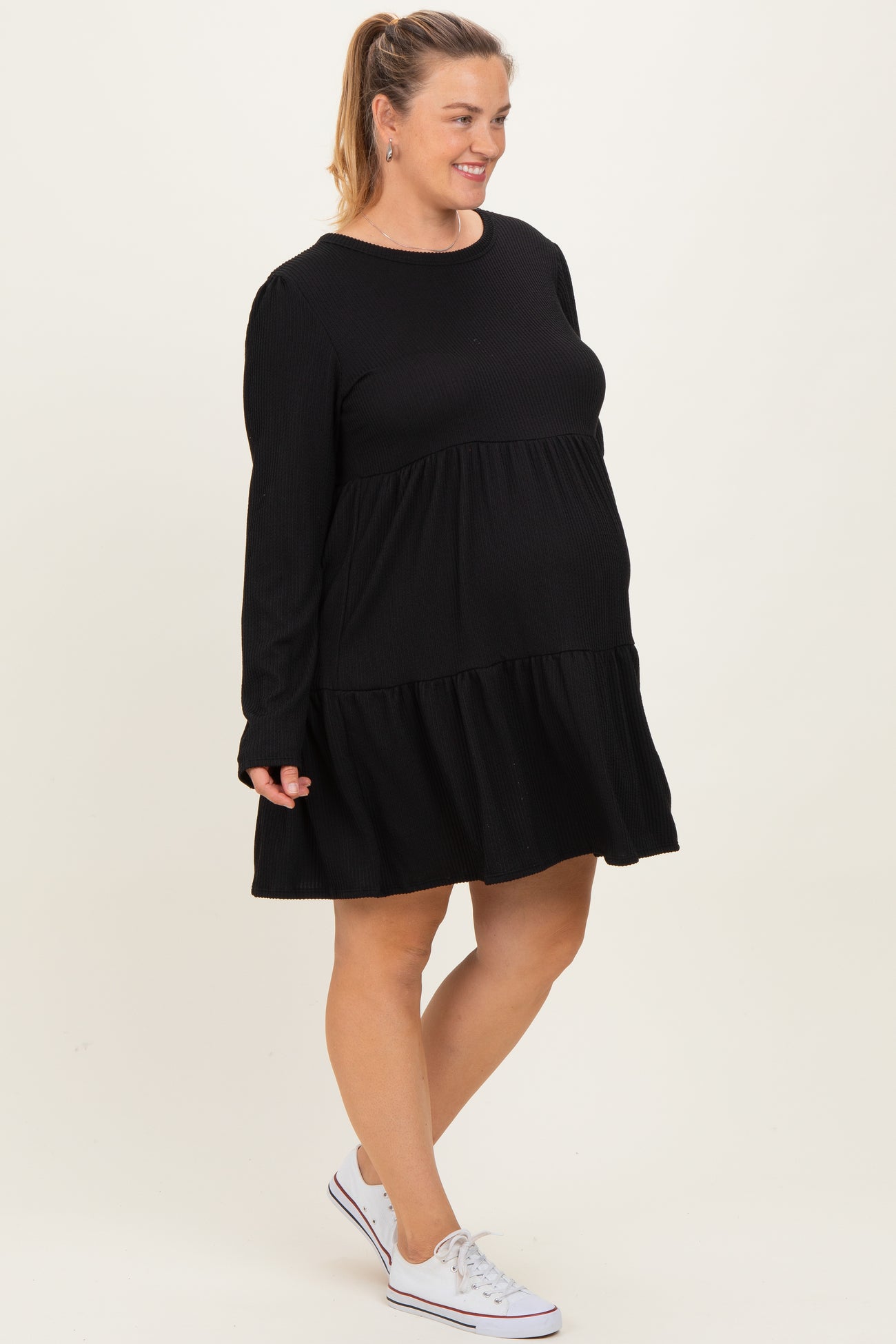 woman wearing a black long sleeve maternity dress with tiered ruffles and a visible baby bump