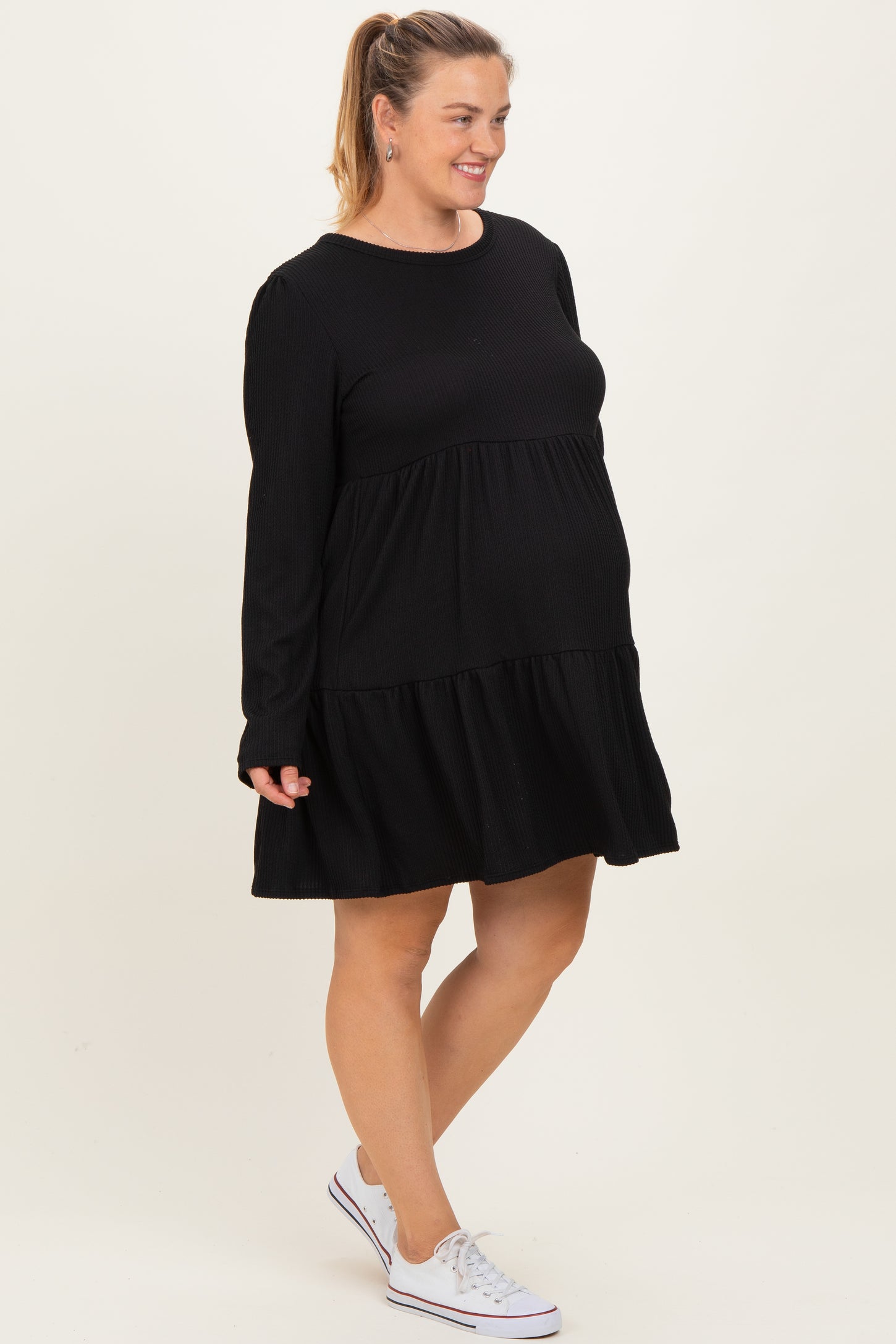woman wearing a black long sleeve maternity dress with tiered ruffles and a visible baby bump