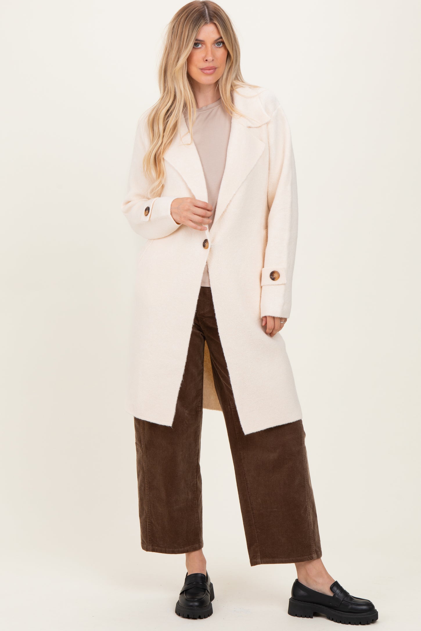 woman wearing a pale pink long cardigan with large buttons, paired with a beige top and brown wide-leg pants