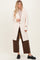 woman wearing a pale pink long cardigan with large buttons, paired with a beige top and brown wide-leg pants