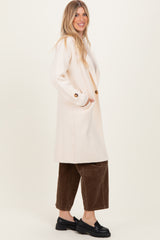woman wearing a long cream-colored cardigan with buttons and side pockets, paired with brown corduroy pants and black shoes
