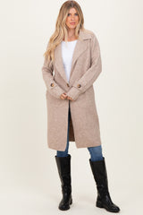 woman wearing a tan long sleeve coat with a wide collar, paired with a white top, blue jeans, and black knee-high boots