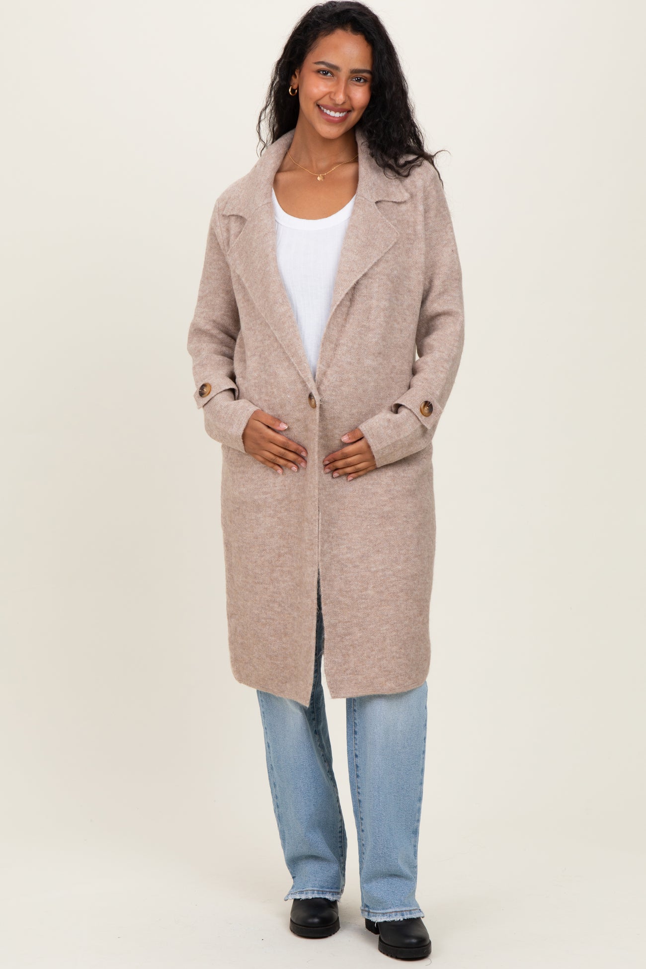 woman wearing a beige maternity coat with an open front and side buttons, holding her baby bump