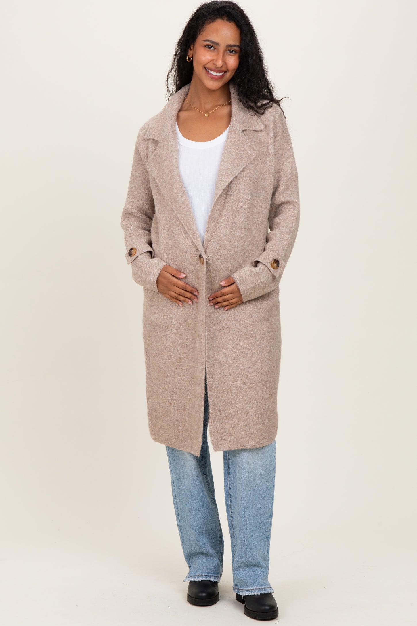 woman wearing a beige maternity coat with an open front and side buttons, holding her baby bump