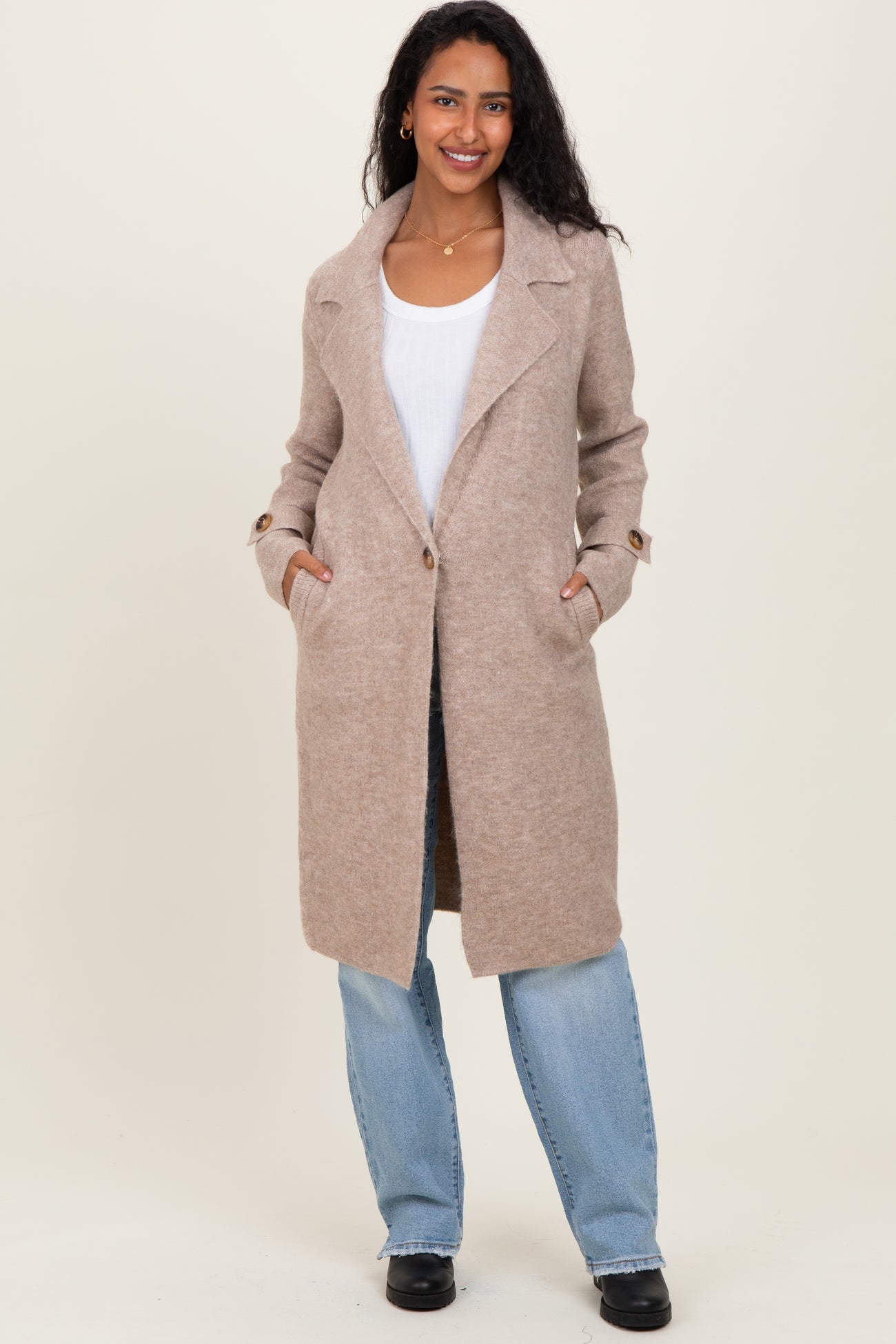 woman wearing a beige long wool blend maternity coat with pockets and a relaxed fit over a white top and blue jeans