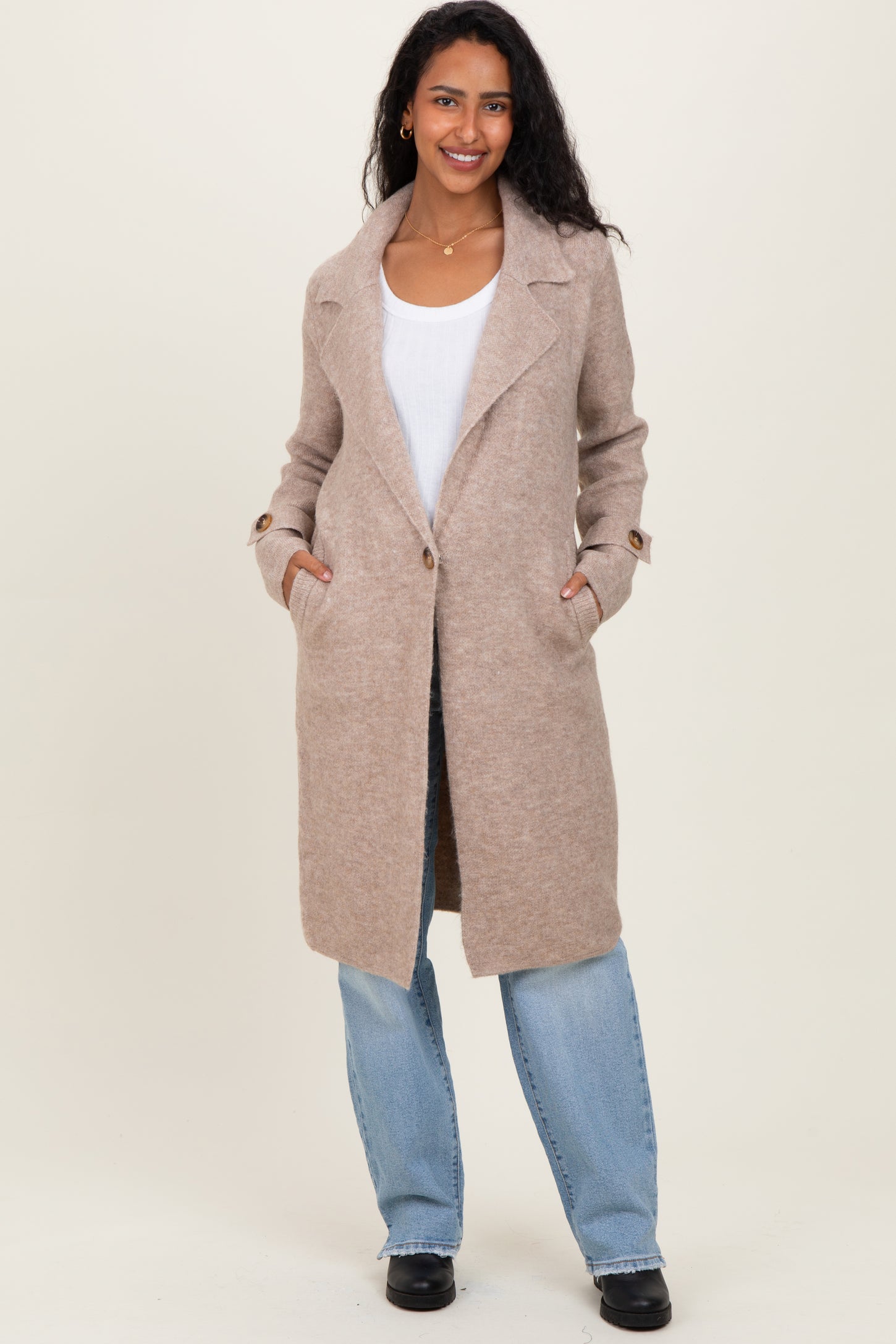 woman wearing a beige long wool blend maternity coat with pockets and a relaxed fit over a white top and blue jeans