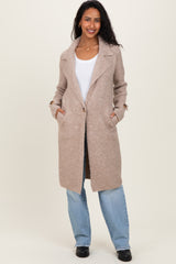woman wearing a beige long wool blend maternity coat with pockets and a relaxed fit over a white top and blue jeans