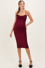 woman wearing a burgundy maternity dress with a ruched design and thin straps, showcasing her baby bump