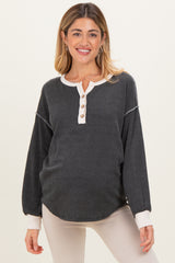 woman wearing a black and cream striped maternity top with button details and long sleeves, showcasing her baby bump