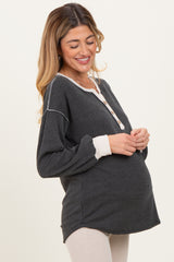 woman wearing a dark gray maternity top with buttons and light gray cuffs, exposing baby bump