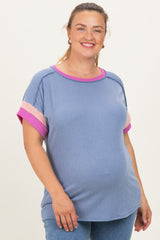 woman wearing a blue ribbed maternity top with pink and coral striped sleeves and a visible baby bump