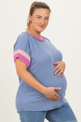 woman wearing a blue striped maternity top with pink accent sleeves and holding her baby bump