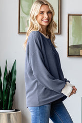 woman wearing a navy blue oversized ribbed sweater with cream cuffs and smiling in a bright room