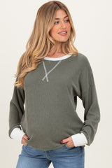 woman wearing a dark green ribbed maternity top with white cuffs and a relaxed fit, smiling at the camera