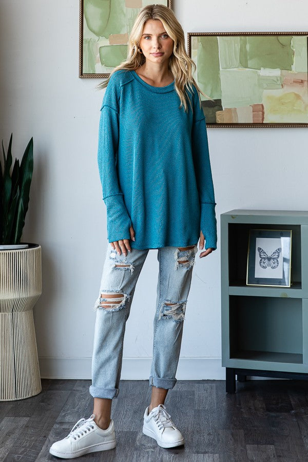 woman wearing a teal oversized waffle knit top and ripped light wash jeans with white sneakers
