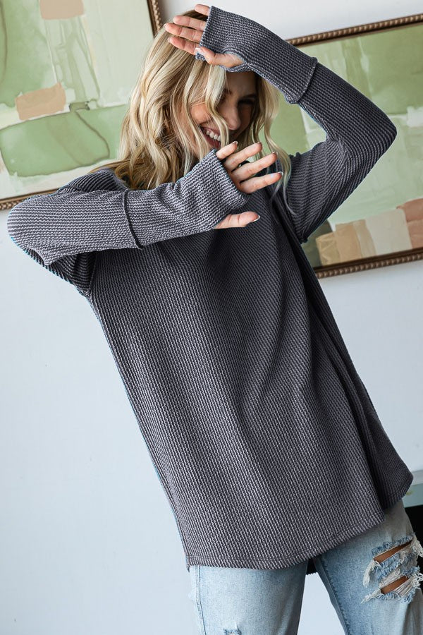 woman wearing a loose-fitting gray ribbed long sleeve top with thumbholes and distressed jeans
