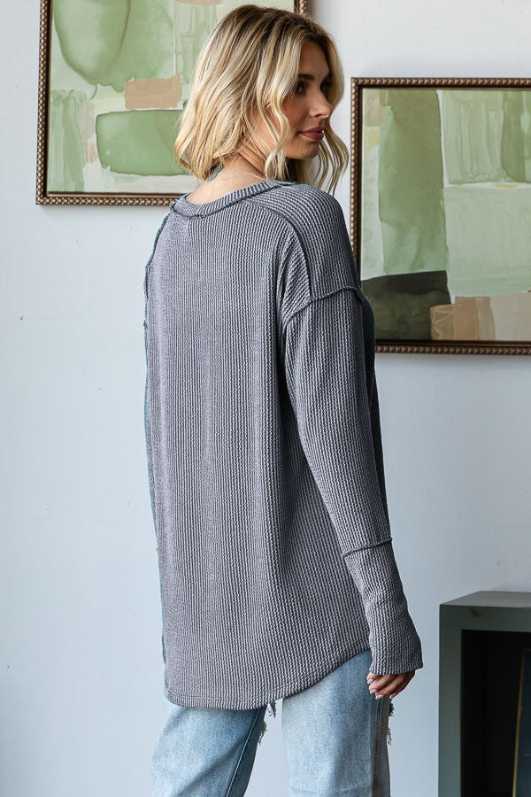woman wearing a gray ribbed long sleeve top with a relaxed fit and side slits, paired with distressed jeans