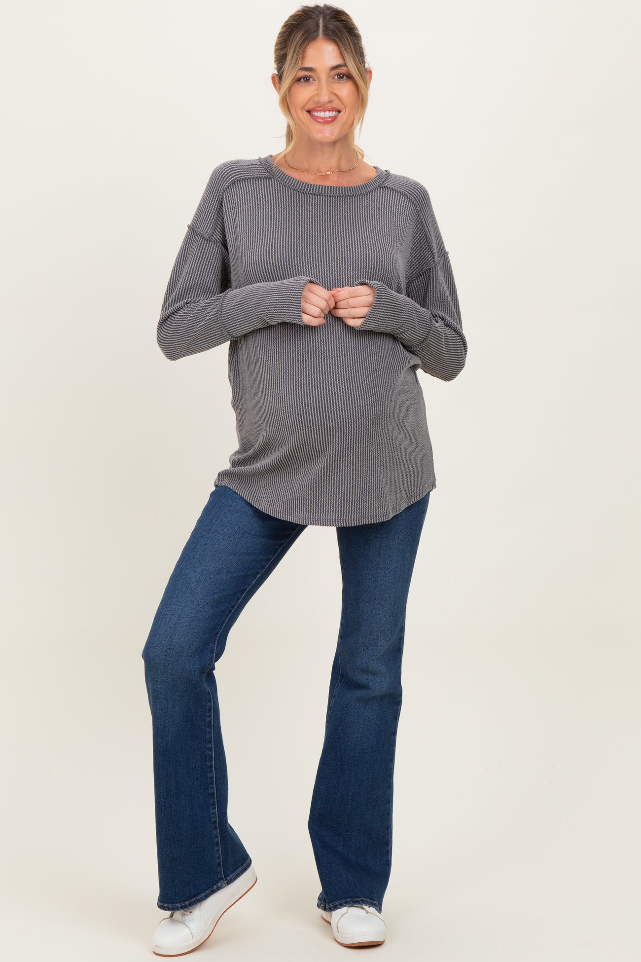 woman wearing a gray striped maternity top and blue flared jeans, showing her baby bump