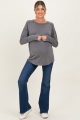 woman wearing a gray striped maternity top and blue flared jeans, showing her baby bump