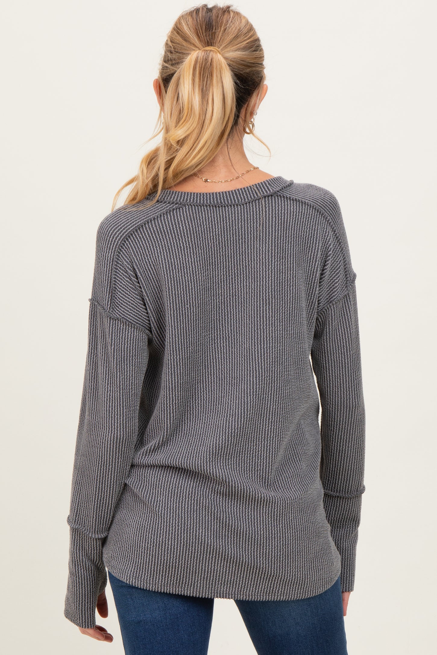 woman wearing a gray ribbed maternity sweater, seen from the back, styled with long sleeves and a loose fit