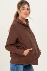 woman wearing a brown maternity hoodie with buttons and a front pocket, showing her baby bump