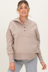 woman wearing a beige maternity hoodie with a buttoned henley neckline and front pocket, styled with gray leggings