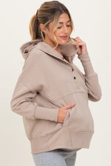 woman wearing a beige maternity hoodie with buttons and a kangaroo pocket, showing a baby bump