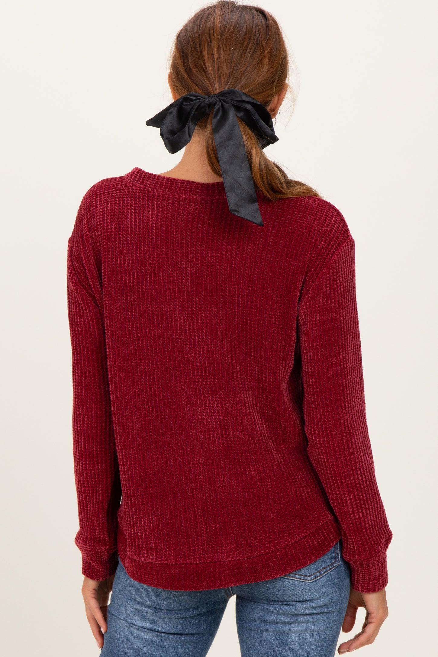 woman wearing a burgundy ribbed sweater with a relaxed fit and a black ribbon in her hair, seen from the back