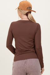 woman wearing a form-fitting brown long sleeve top, viewed from the back, with a brown cap and styled hair