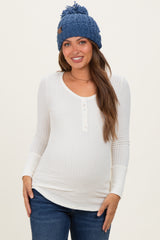 woman wearing a white long sleeve maternity top with buttons and a baby bump, paired with a blue knitted beanie and jeans