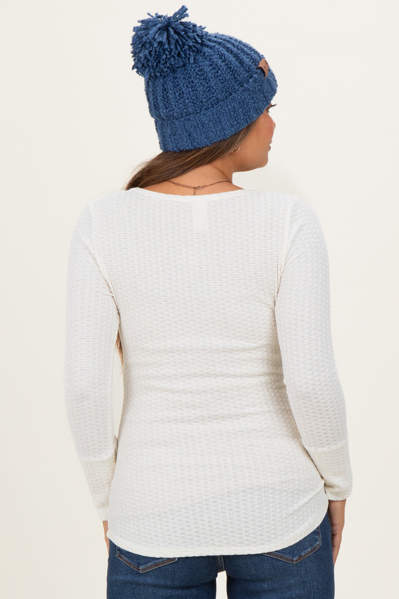 woman wearing a white long sleeve maternity top with a textured design and a blue knit beanie