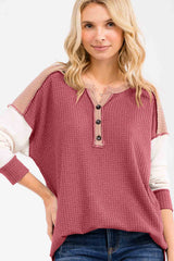 woman wearing a burgundy henley top with beige accents and button detail, styled with loose-fitting sleeves