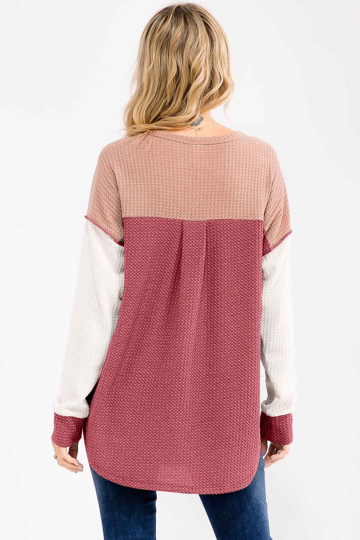 woman wearing a color-blocked long sleeve top in burgundy, beige, and cream with a curved hem and relaxed fit