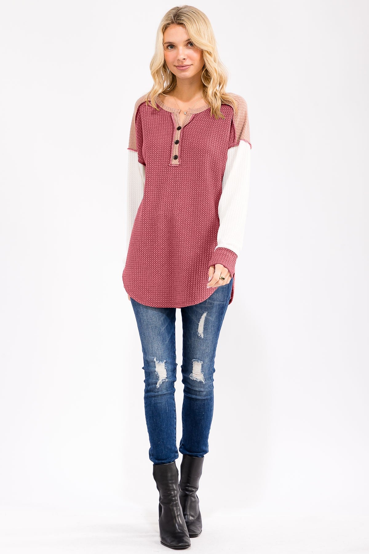 woman wearing a burgundy and cream long sleeve waffle knit top with button details, paired with distressed blue jeans and black boots