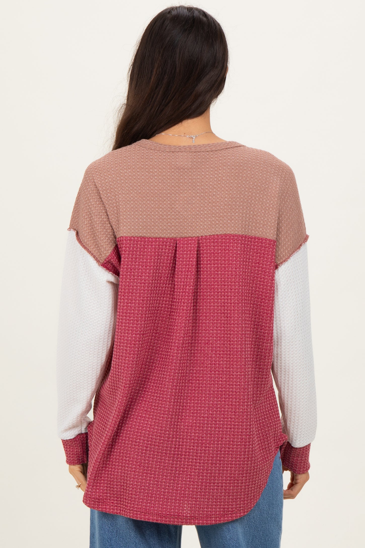 woman wearing a color block long sleeve top in mauve, white, and rose from the back, featuring a relaxed fit