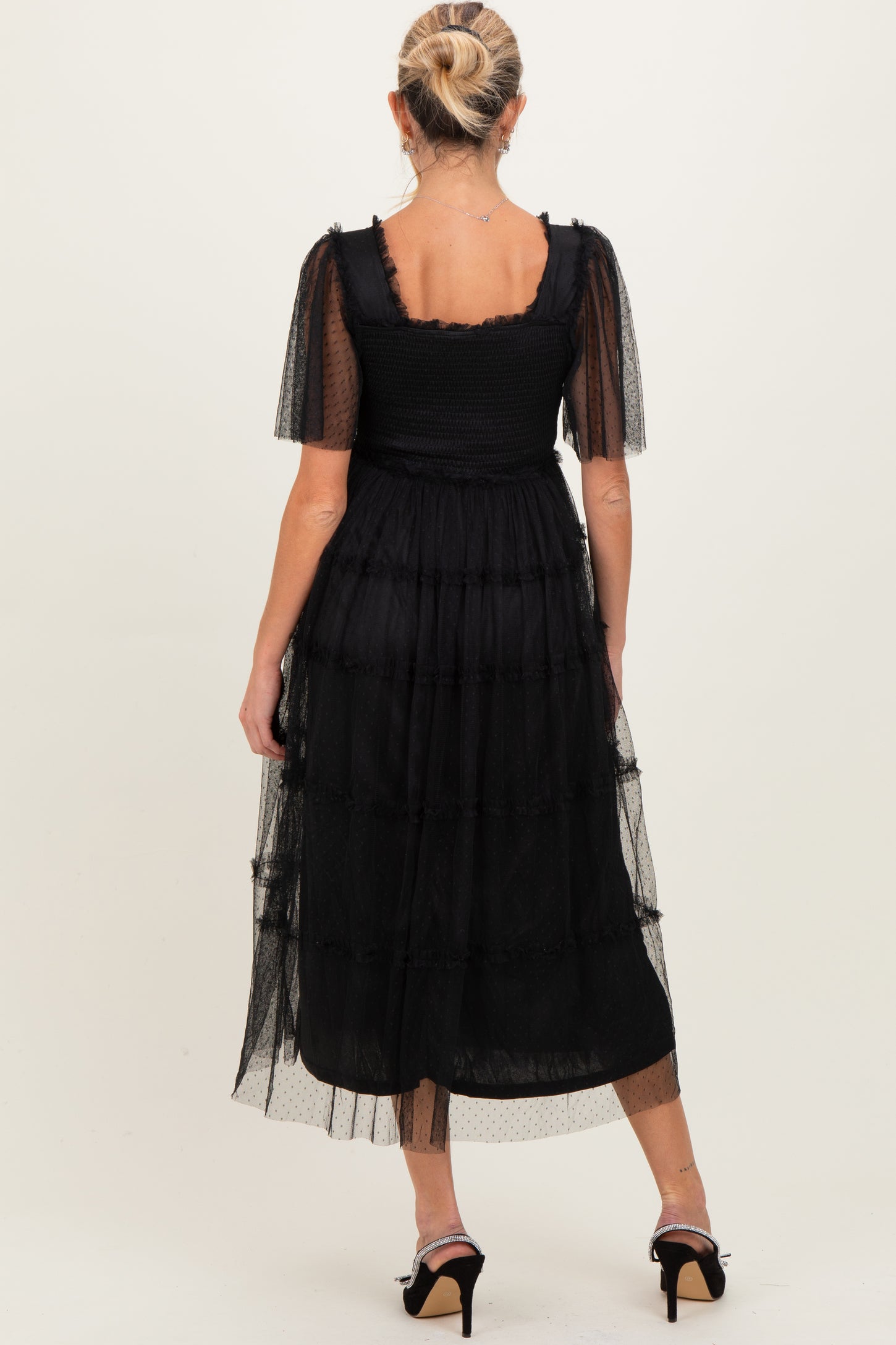 woman wearing a black maternity dress with short puff sleeves and tiered tulle skirt, showing a baby bump from the back