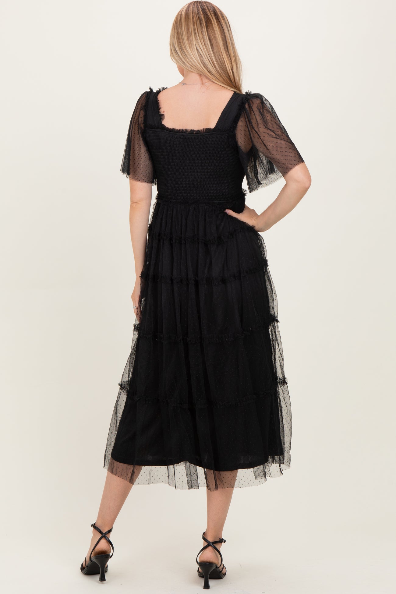 woman wearing a black tiered midi dress with sheer puff sleeves and a smocked bodice, shown from the back