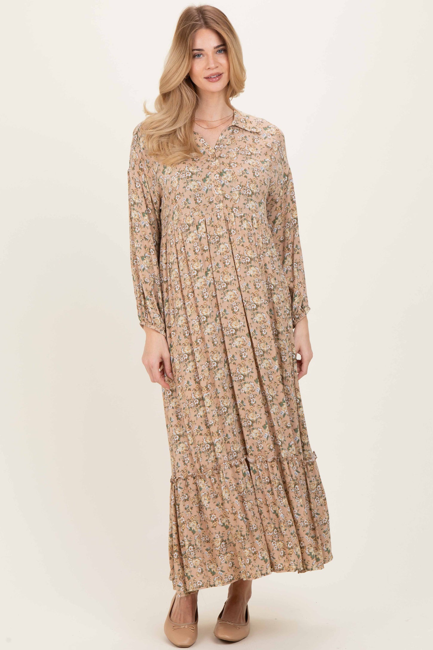 woman wearing a long-sleeve floral maxi dress in shades of beige and pink with a tiered skirt