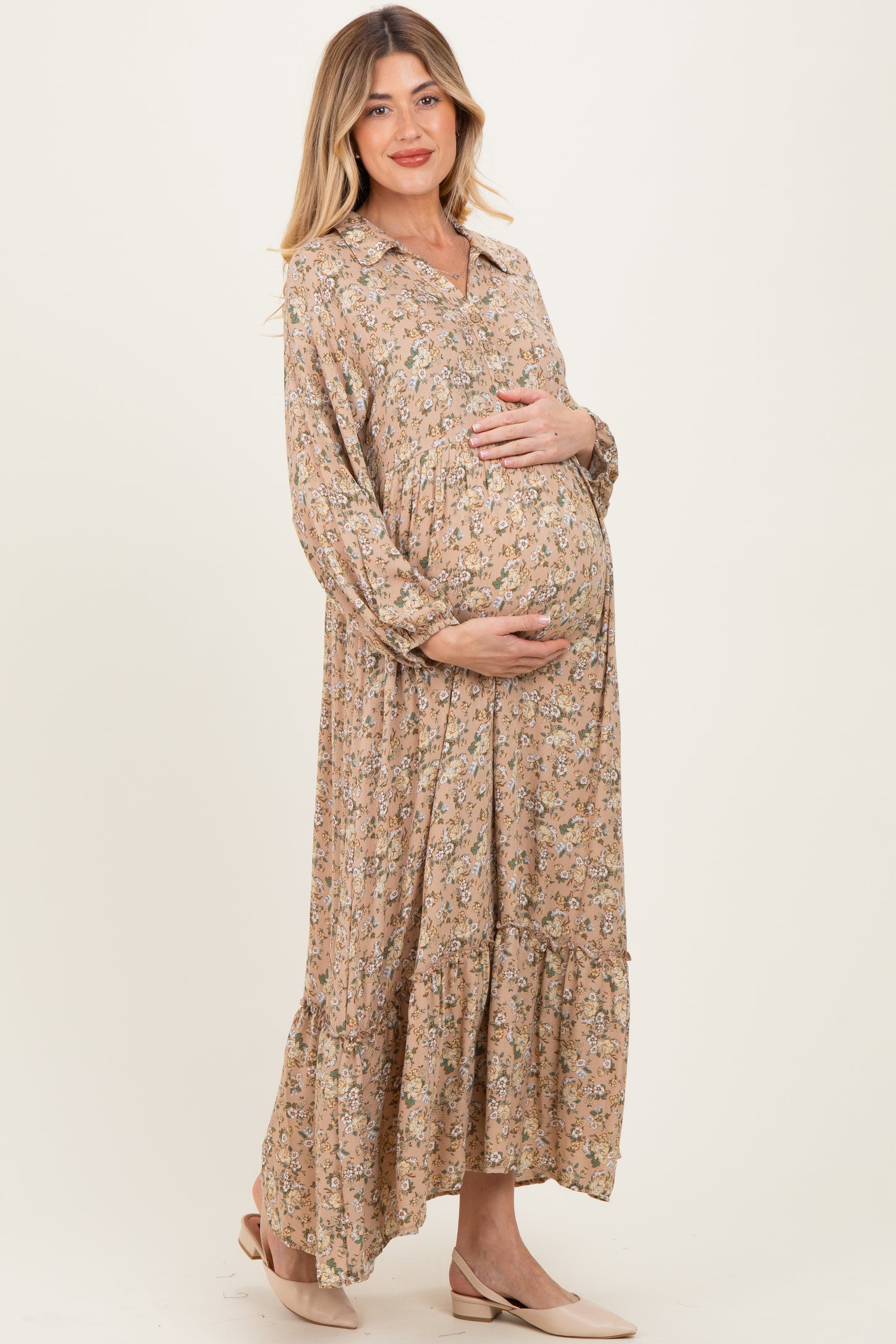 woman wearing a floral maternity dress with a tiered skirt and holding her baby bump