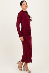 woman wearing a burgundy long sleeve fitted dress with ruching and a side slit, paired with silver high heels