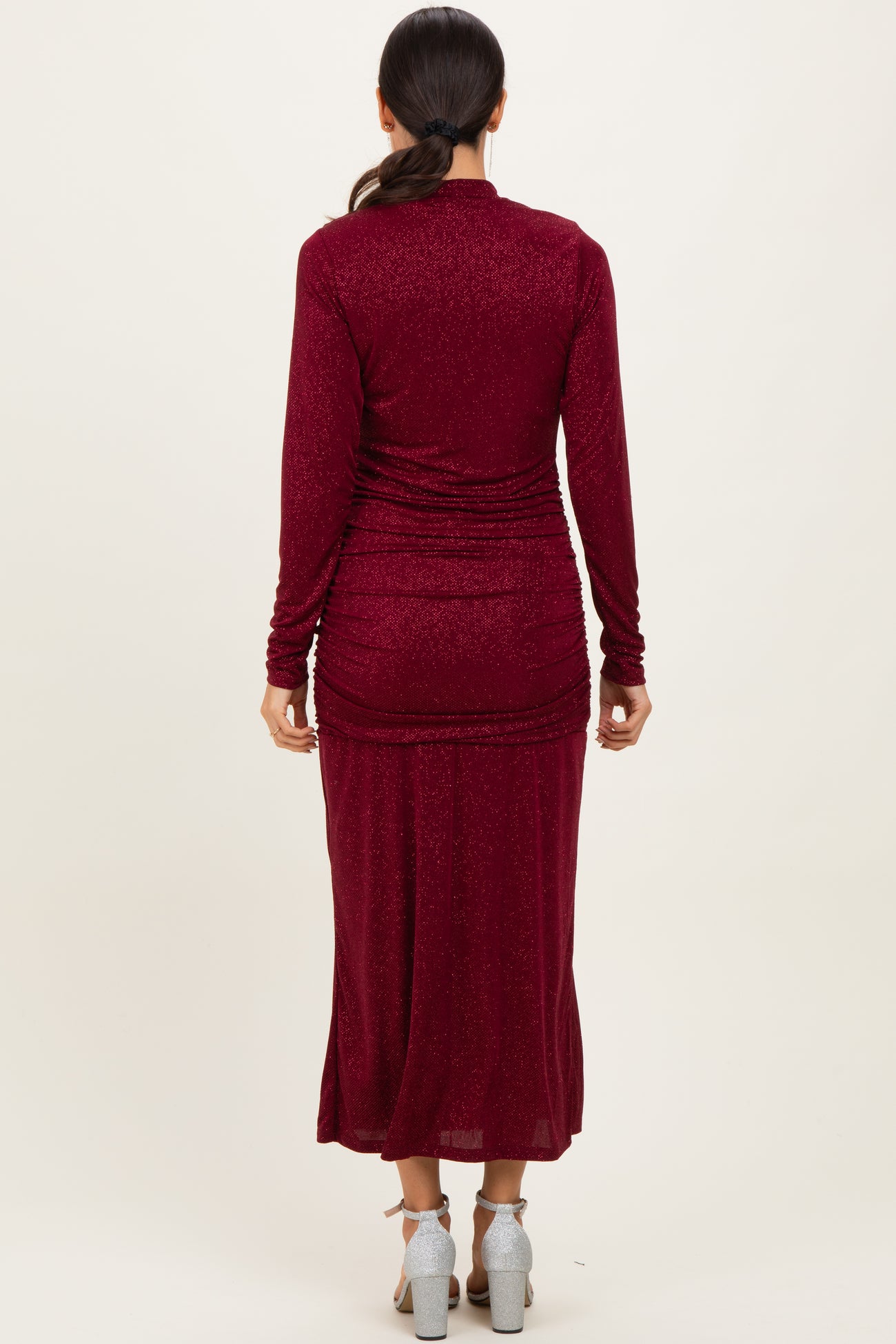 woman wearing a burgundy long sleeve shimmer maxi dress with a ruched back detail and high slit