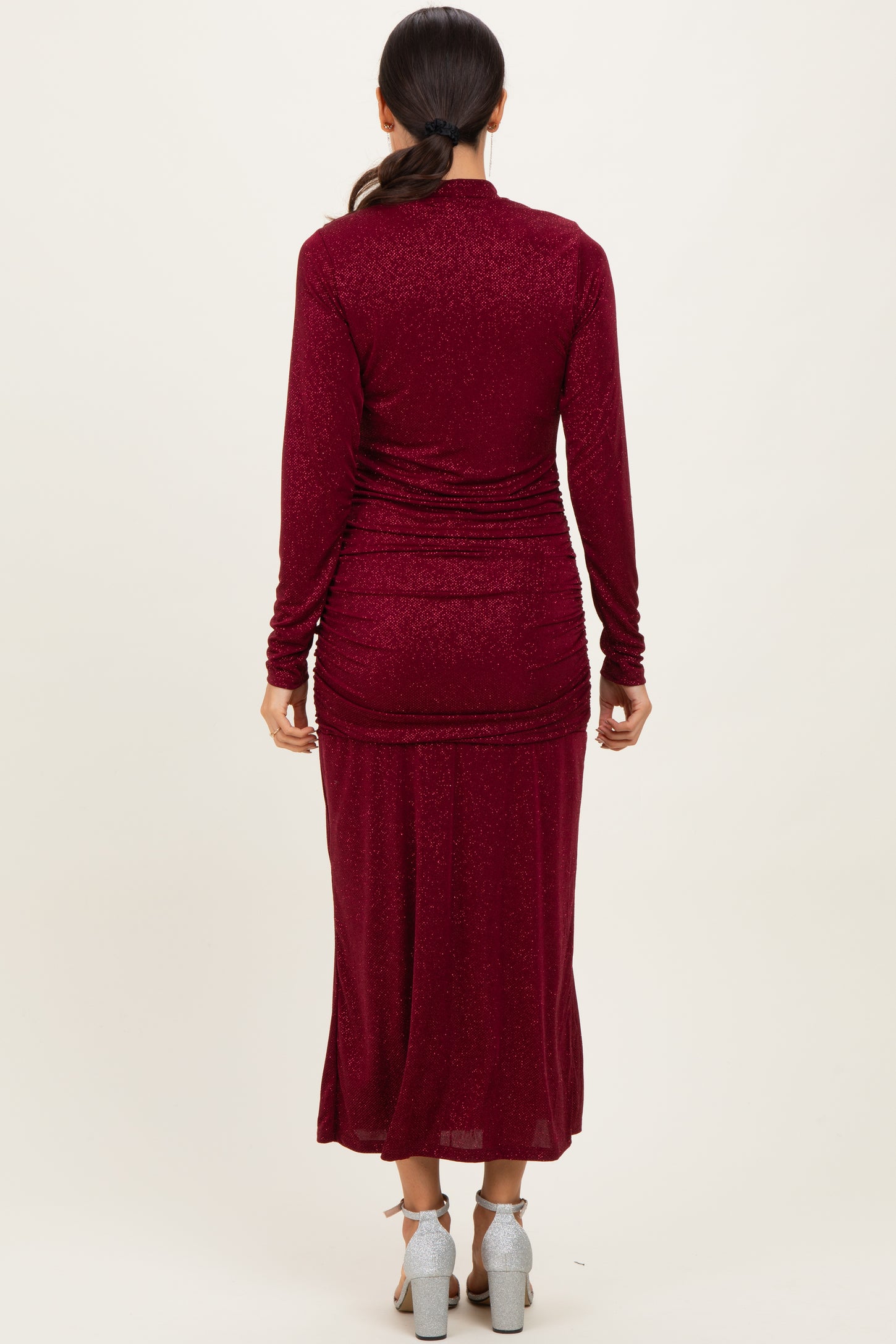 woman wearing a burgundy long sleeve shimmer maxi dress with a ruched back detail and high slit