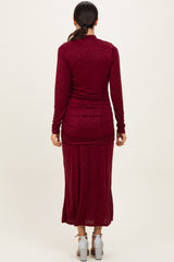 woman wearing a burgundy long sleeve shimmer maxi dress with a ruched back detail and high slit