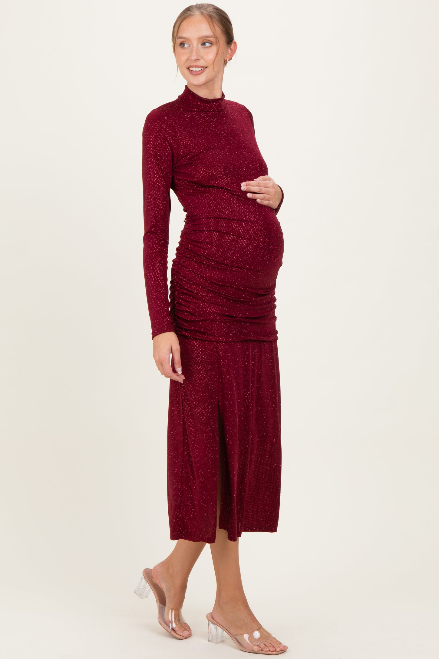 woman wearing a burgundy long sleeve maternity dress with ruched details and a side slit, showing her baby bump
