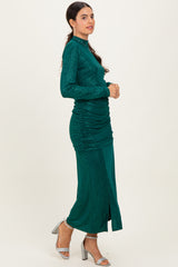woman wearing a teal glittered long sleeve dress with ruched detailing and a side slit, standing in profile