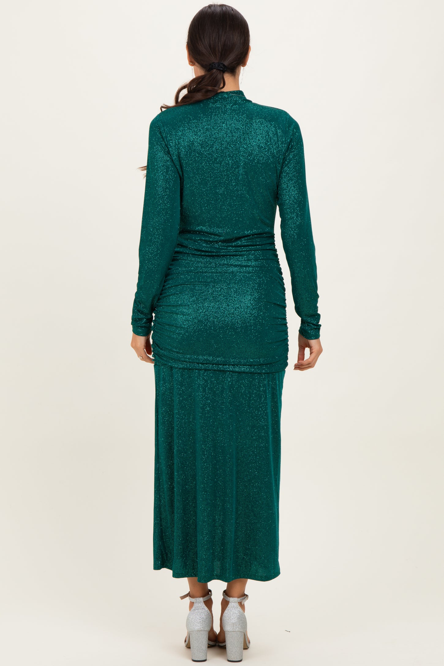 woman wearing a dark green long sleeve glittery maxi dress, view from the back showing ruching details